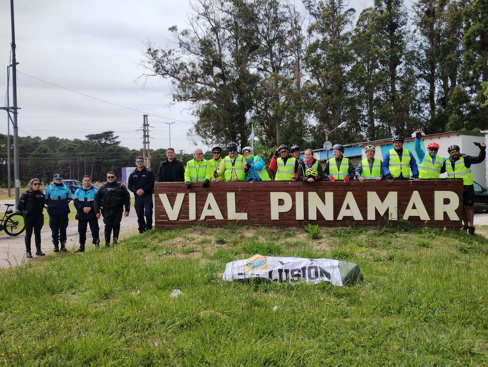 El grupo Atreverse con cascos y chalecos reflectivos frente al cartel de madera de Pinamar, con una bandera que dice Por más INCLUSIÓN
